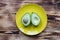 Avocado on a yellow plate, green avocado fruit cut in half, a large stone on a brown wooden table