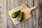 Avocados on natural pine cutting board on wooden background. Two whole green fresh tropical fruits on brown table, top view