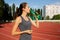 Awesome brunette woman drinking water during running at the stadium. Space for text