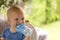 Awesome curly blondy toddler sitting outdoor and drinking water.