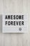 `Awesome forever` word on modern board on a white wooden surface, top view. From above, flat lay, overhead