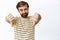 Awful, dislike. Disappointed caucasian man with beard, showing thumbs down and looking displeased, standing in t-shirt