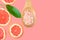 Ayurveda face skin scrub ingredients Himalayan salt in wooden spoon sliced grapefruit green leaf on cherry pink background