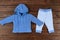 Babies blue knitted cardigan and striped pants on wooden background. Baby clothes