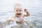 Baby bathes splashing water and mom supports daughter by hand