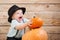 Baby in black hat with pumpkins on wooden background