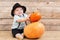 Baby in black hat with pumpkins on wooden background