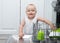 Baby blonde boy with blu eyes helping in the kitchen using dishwasher. white kitchen interior.
