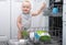 Baby blonde boy with blu eyes helping in the kitchen using dishwasher. white kitchen interior.