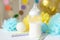 Baby bottle with breast milk, various festive paper decor in front of baby bed. It`s a boy or baby birthday celebration concept.