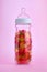 Baby bottle containing colorful jellies on pink background