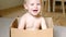 Baby in the Box. Pretty baby infant girl sitting inside a Cardboard box. Baby toddler in a carton box playing, smiling