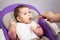 Baby boy first feeding, little child sitting in chair in domestic room, female hand with spoon