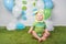 Baby boy in holiday Easter bunny rabbit costume with large ears, dressed in green clothes onesie, sitting on rug