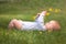 Baby boy is lying on green gras and playing with yellow flower