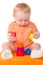 Baby boy in orange playing with toy pyramid