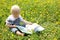 Baby Boy reading book in dandelions