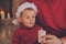 Baby boy in red Santa Claus hat blows candle.