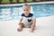 Baby boy sitting dangerously on the edge of a swimming pool