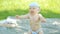 Baby boy sitting near basin in green garden. Beautiful baby smiling, hits the water rises and sets