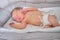 A baby boy sleeps in a cocoon on a cot. A newborn baby in a diaper is lying naked on the bed