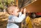 Baby boy standing near metal fence in autumn yard