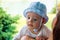 Baby in cap on little head with fascinated face and focused blue eyes resting above motherâ€™s shoulder outside in nature