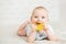 Baby chewing Teether Toy lying down on Stomach in White Bedroom. Child sucking Nibbler and massaging Gums. Babies teething. Cute