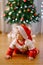 Baby in a Christmas costume and Santa hat is crawling in front of a Christmas tree
