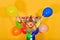 Baby clown holds hands to the sides with balloons on a yellow background