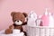 Baby cosmetic products in wicker basket, bath accessories and knitted toy bear on pink background