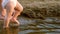 Baby in diaper takes first steps along river bank, sprinkling water around and walking with her mother. Legs. Slow