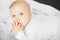 Baby with dreamy look lies on bed with finger in mouth