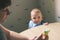 Baby eating food on kitchen. Mom is going to feed the child.