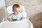 Baby eating vegetables. green cucumber in little girl hand in sunny kitchen. Healthy nutrition for kids. Solid food for infant.