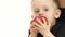 Baby eats an apple, next to her mother. White background. Slow motion. Close up