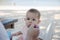 Baby eats porridge, soiled and food in the nose. Dad feeds little daughter with a spoon. Against the backdrop of a tropical beach