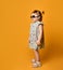 Baby female in sunglasses dressed upside down, gray polka dot dress and white sandals. Posing sideways on orange background