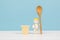 A baby figurine with a wooden spoon and a cup of banana dessert on a wooden table. The concept of healthy baby food