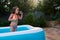 Baby girl in bathing suit blows soap bubbles while sunbathing in an inflatable pool in the backyard garden of the house