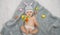 Baby girl in bunny hat lying on gray blanket with multicolored easter eggs