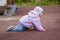 Baby girl crawling on all fours on the playground. A child in warm jeans clothes hat jacket windbreaker. 1 year old baby walks