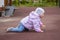 Baby girl crawling on the playground. A child in warm clothes on all fours. A 1 year old baby walks near the house in spring