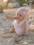 Baby girl in dress on sandy beach gives a pebble. Little girl with sunset tones