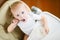 Baby girl in a feeding chair places a spoon with rice porridge in her mouth