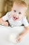 Baby girl in a feeding chair places a spoon with rice porridge in her mouth. Vertical