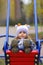 Baby girl in a funny hat swinging on the winter playground, perspective point of view.