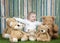 Baby girl with group of teddy bears, seated on grass