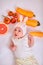 Baby girl in a hat with bunny ears lies on a white background with fruits and vegetables and holds a carrot in her hand - healthy