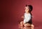 Baby girl in headband, smart white bodysuit, barefoot. She sitting on floor against pink background. New Year, holidays. Close up